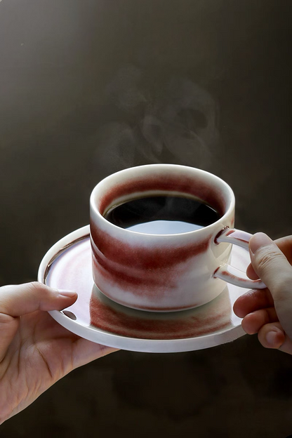 Style 1 ceramic cup and saucer in beige and red held by hand with coffee highlighting everyday usability and comfort grip