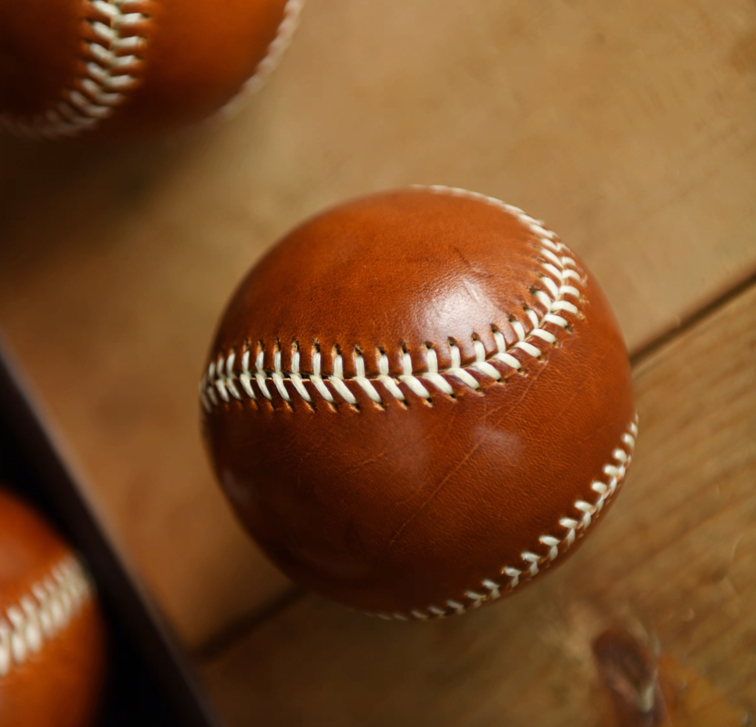 Close-up of caramel leather baseball highlighting natural grain and cream stitching.