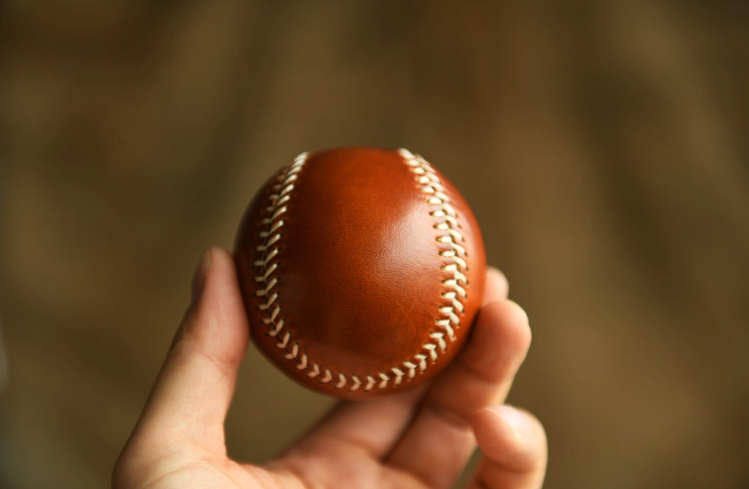 Person holding a caramel full-grain leather baseball in hand, showing scale and finish.