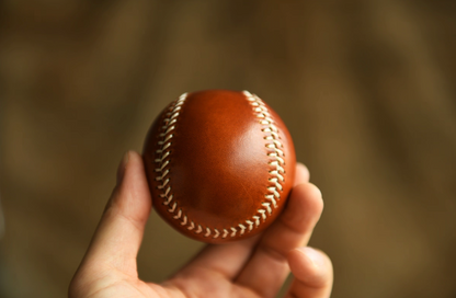 Person holding a caramel full-grain leather baseball in hand, showing scale and finish.