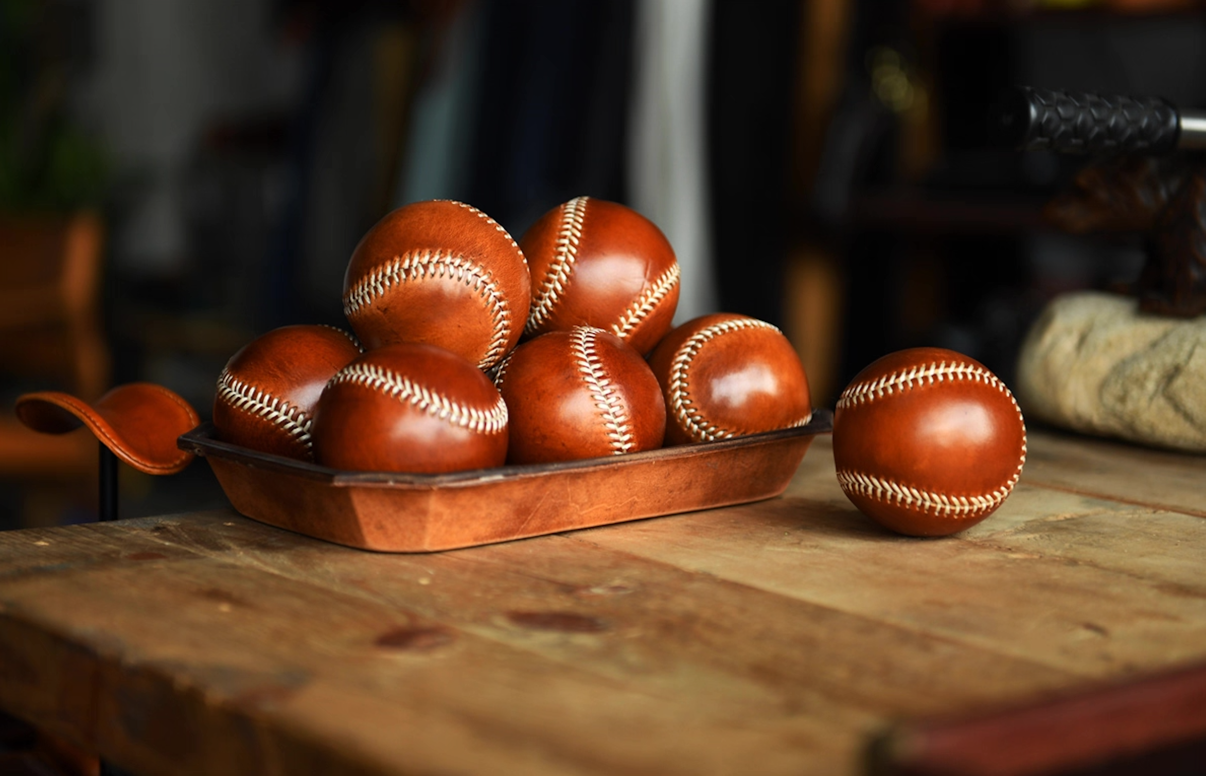 Multiple caramel leather baseballs displayed in a tray on rustic wooden table.