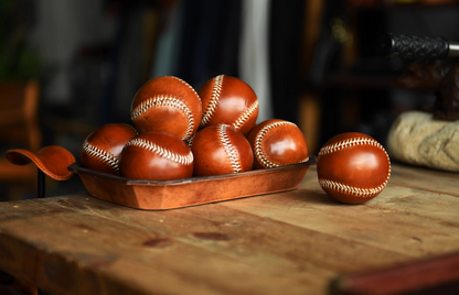 Multiple caramel leather baseballs displayed in a tray on rustic wooden table.