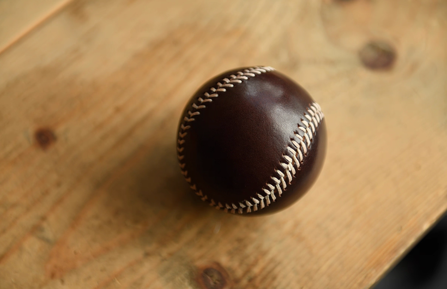 Dark brown handcrafted leather baseball resting on wooden surface under natural light.