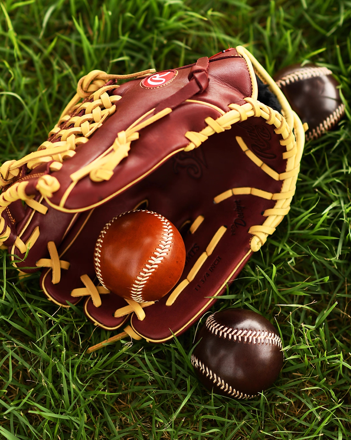 Caramel and dark brown leather baseballs in a classic glove placed on grass field.