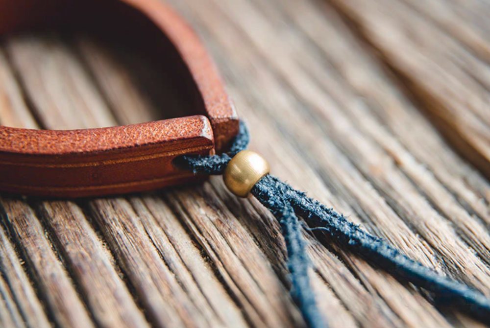 Dark brown handcrafted leather loop bracelet close-up of brass bead and blue suede cord adjustable closure
