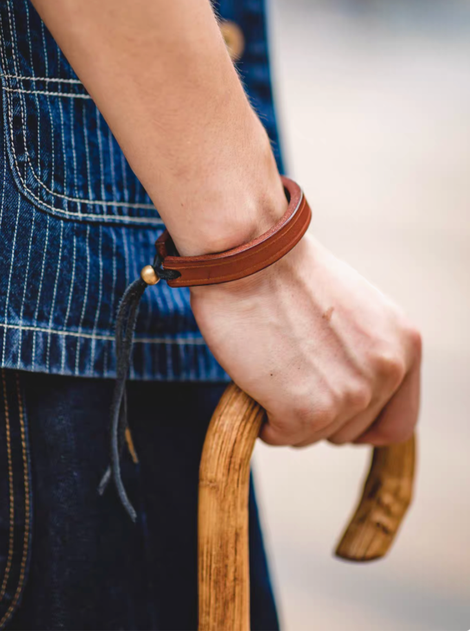 Dark brown handcrafted leather loop bracelet worn on model wrist in close-up with adjustable cord detail