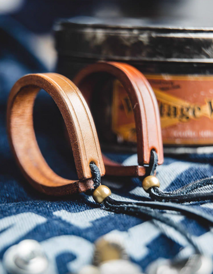 Handcrafted leather loop bracelets in dark brown and original color placed beside leather case showing product texture and craftsmanship