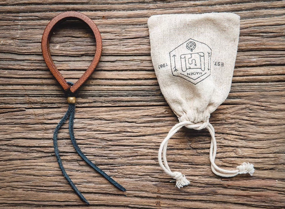 Dark brown handcrafted leather loop bracelet flat lay next to fabric pouch showing single bracelet and adjustable cord