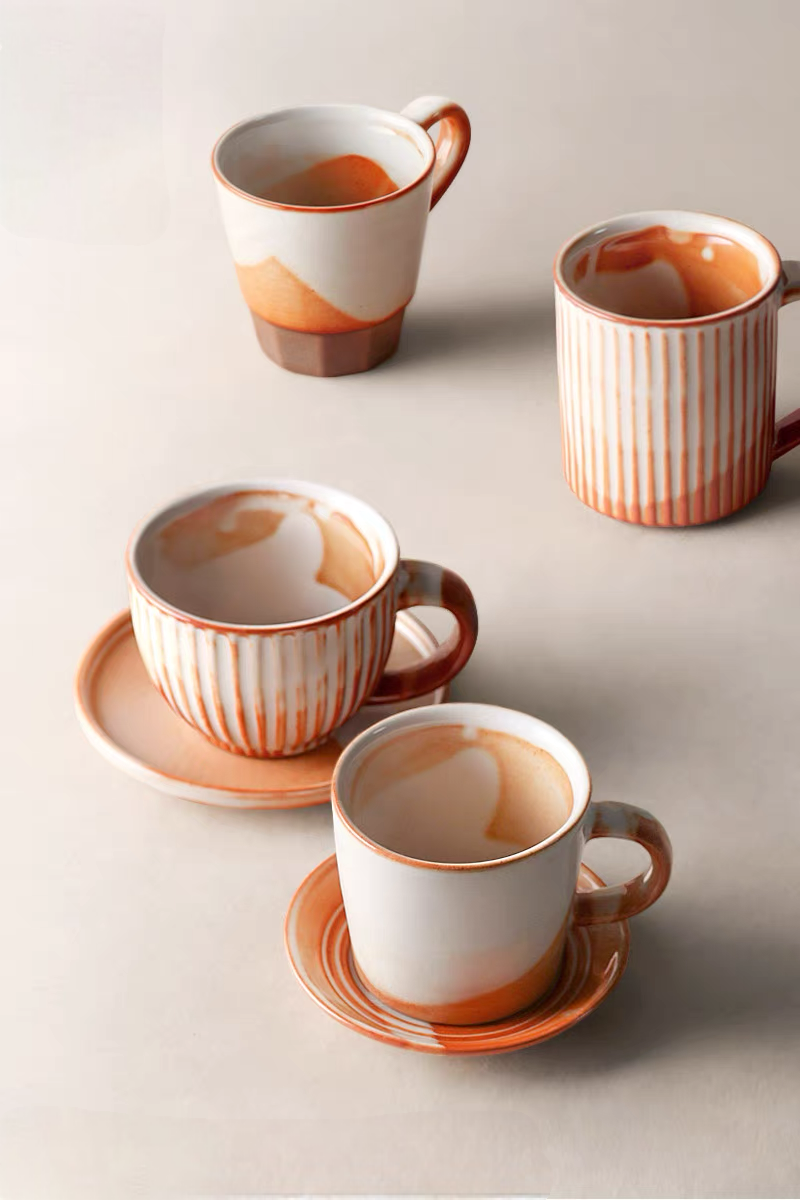Top view of handcrafted vintage ceramic mugs in off-white and orange showing multiple styles with different shapes and glaze patterns