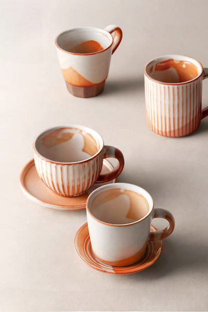 Top view of handcrafted vintage ceramic mugs in off-white and orange showing multiple styles with different shapes and glaze patterns