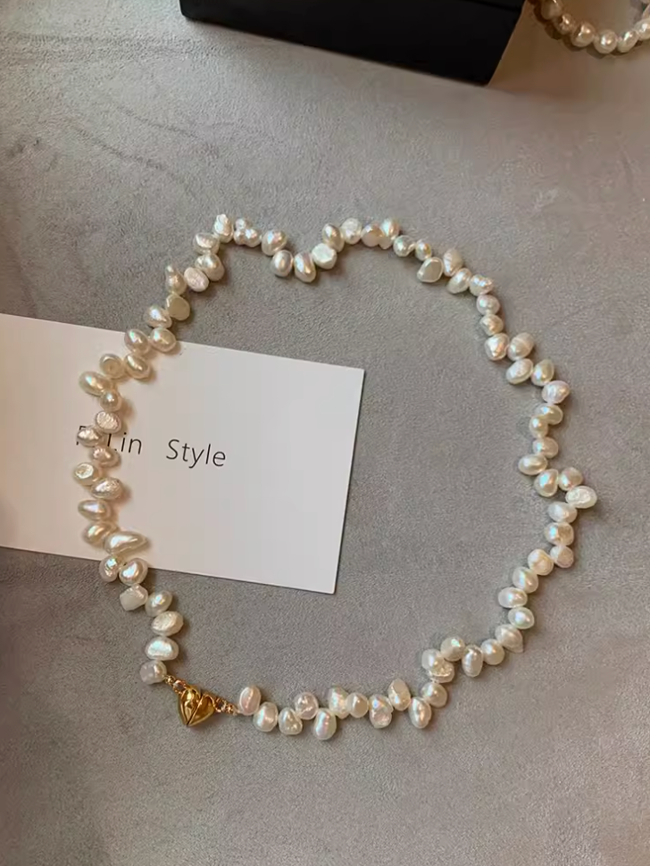 White baroque pearl statement choker with irregular freshwater pearls and 24K gold-plated heart clasp displayed on soft surface