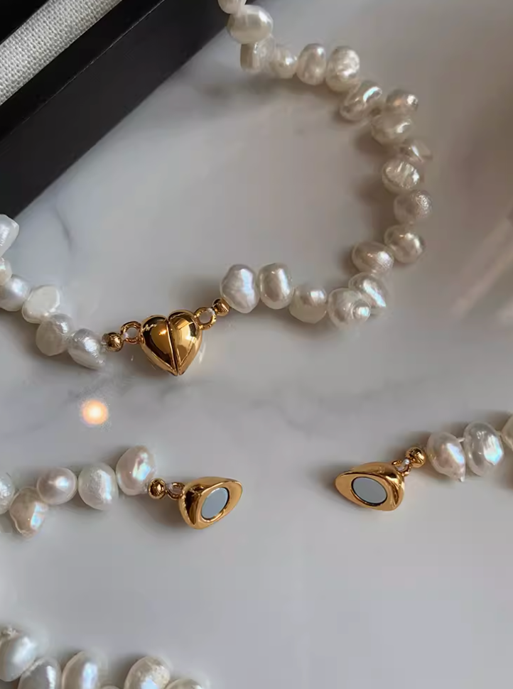 Close-up of white baroque pearl necklace showing irregular freshwater pearls and polished 24K gold-plated heart clasp detail