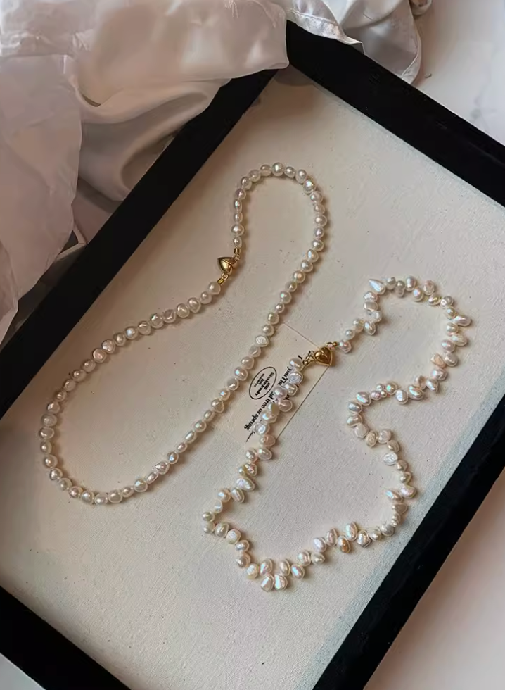 White baroque pearl choker with irregular pearls compared with classic round pearl necklace, both featuring gold heart clasps