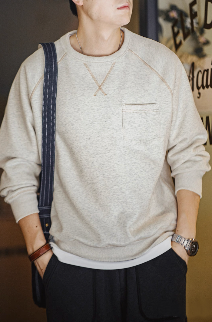 Model wearing gray fleece sweatshirt indoors with black pants and watch, casual styling.