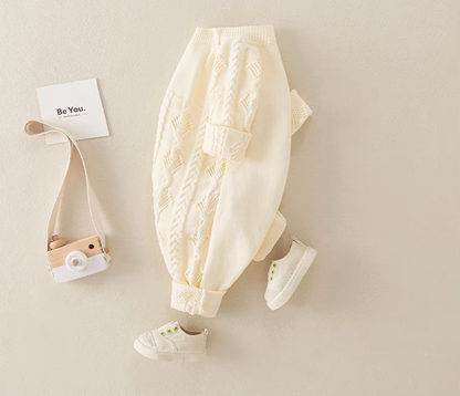 Beige cable knit baby romper laid flat at an angle with baby shoes and soft neutral styling