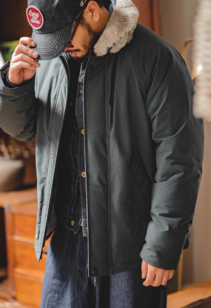 Model tipping cap while wearing slate blue bomber jacket with fur collar.
