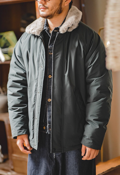 Model wearing slate blue flight jacket indoors, hands in pockets, front view.