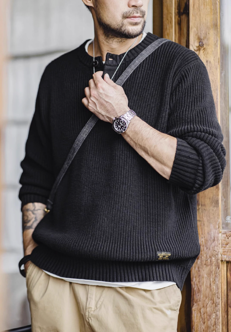 Model standing by wooden door wearing black Henley knit sweater.