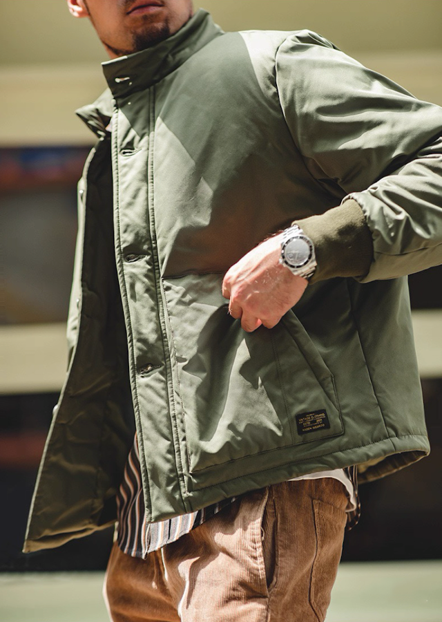 Army green padded jacket on model, front angle while opening placket.