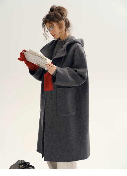 Model wearing Highland Wool Toggle Coat in dark gray reading a book, featuring hooded design, toggle closure, mid-length silhouette, and relaxed fit