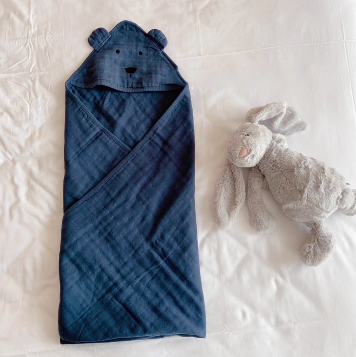 Bear Navy Blue hooded cotton muslin baby swaddle wrap fully wrapped on bed with plush toy showing cozy design