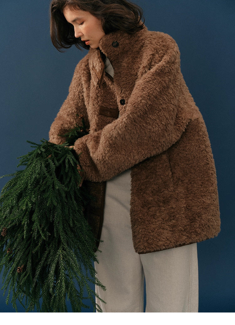 Mid-shot of model adjusting chocolate teddy coat while holding pine greenery.