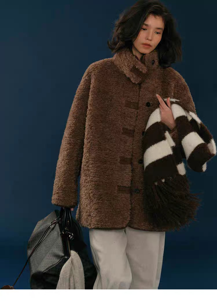 Walking shot of model in chocolate teddy wool-blend coat with striped scarf and travel bag.