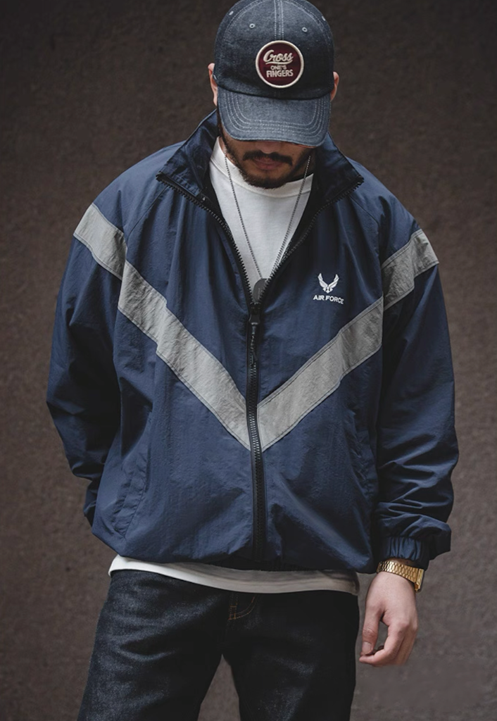 Model wearing navy blue AIR FORCE training jacket zipped up with reflective stripes.