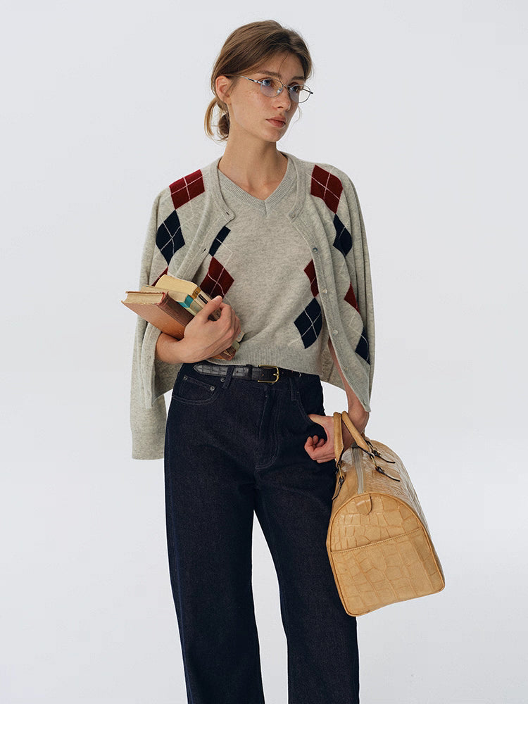 Oat beige wool argyle cardigan draped over shoulders with matching V-neck sweater, styled with dark denim and books.