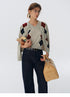 Oat beige wool argyle cardigan draped over shoulders with matching V-neck sweater, styled with dark denim and books.