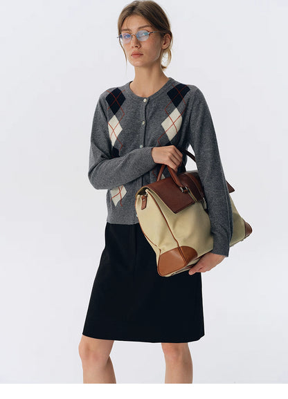 Full-body view of charcoal gray argyle wool button-up cardigan styled with a black skirt and tan travel bag.