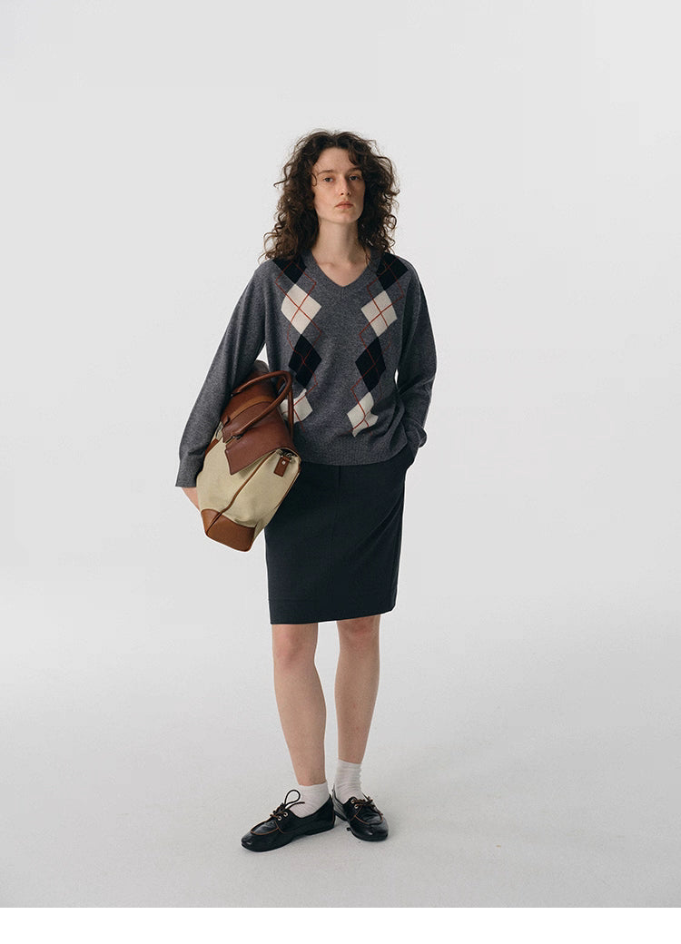 Full body shot of charcoal V-neck argyle wool sweater styled with dark skirt and leather bag.