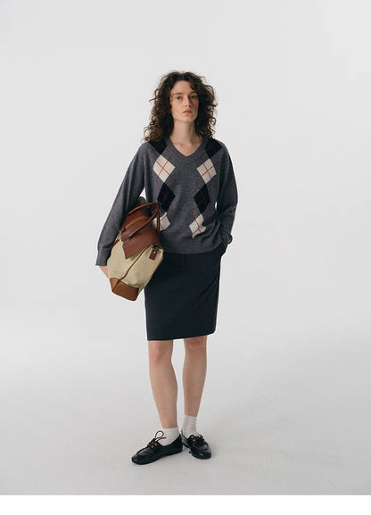 Full body shot of charcoal V-neck argyle wool sweater styled with dark skirt and leather bag.