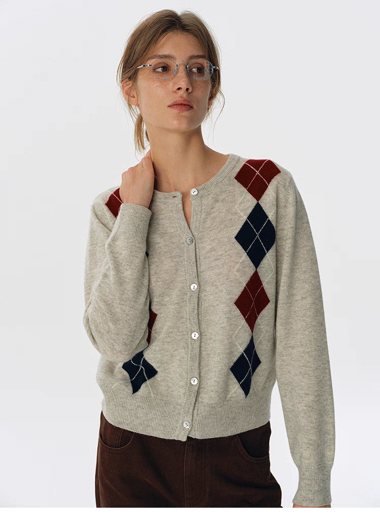 Front view of oat beige wool argyle button-up cardigan, worn with brown pants and glasses.