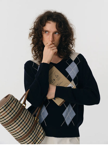 Model holding a mailer while wearing navy argyle V-neck wool sweater and plaid duffle bag.