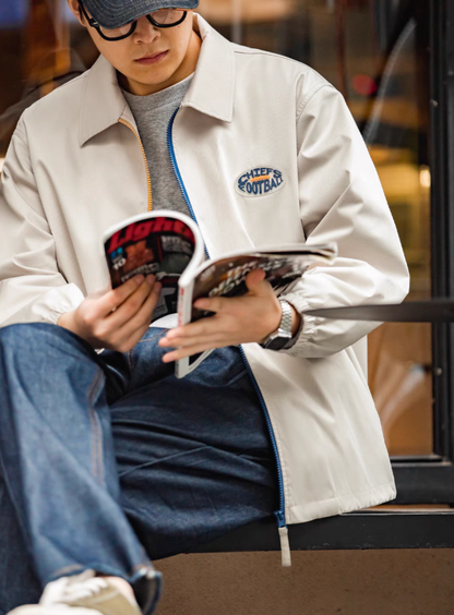 Model sitting and reading while wearing off-white coach jacket, casual look.