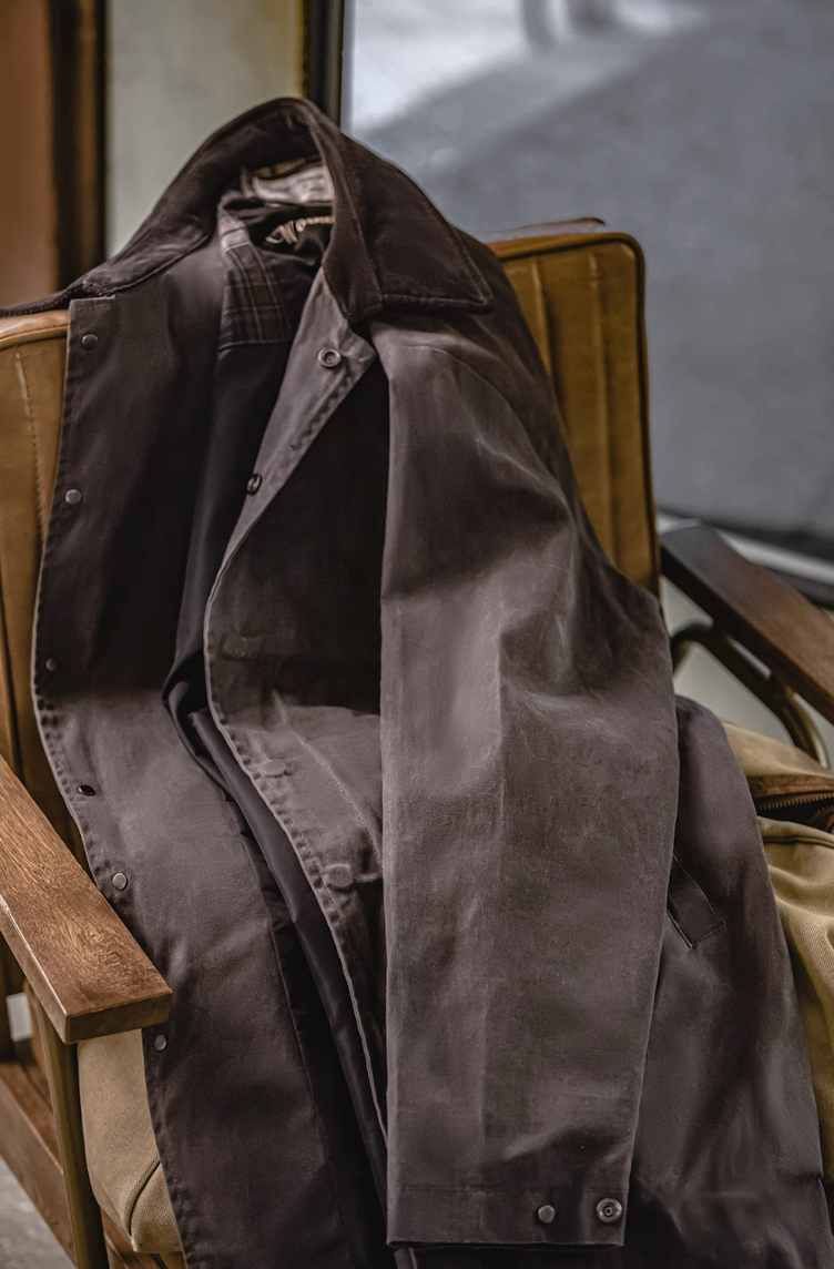 Brown waxed cotton coat displayed casually on chair