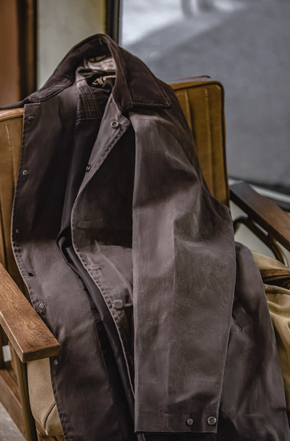 Brown waxed cotton coat displayed casually on chair