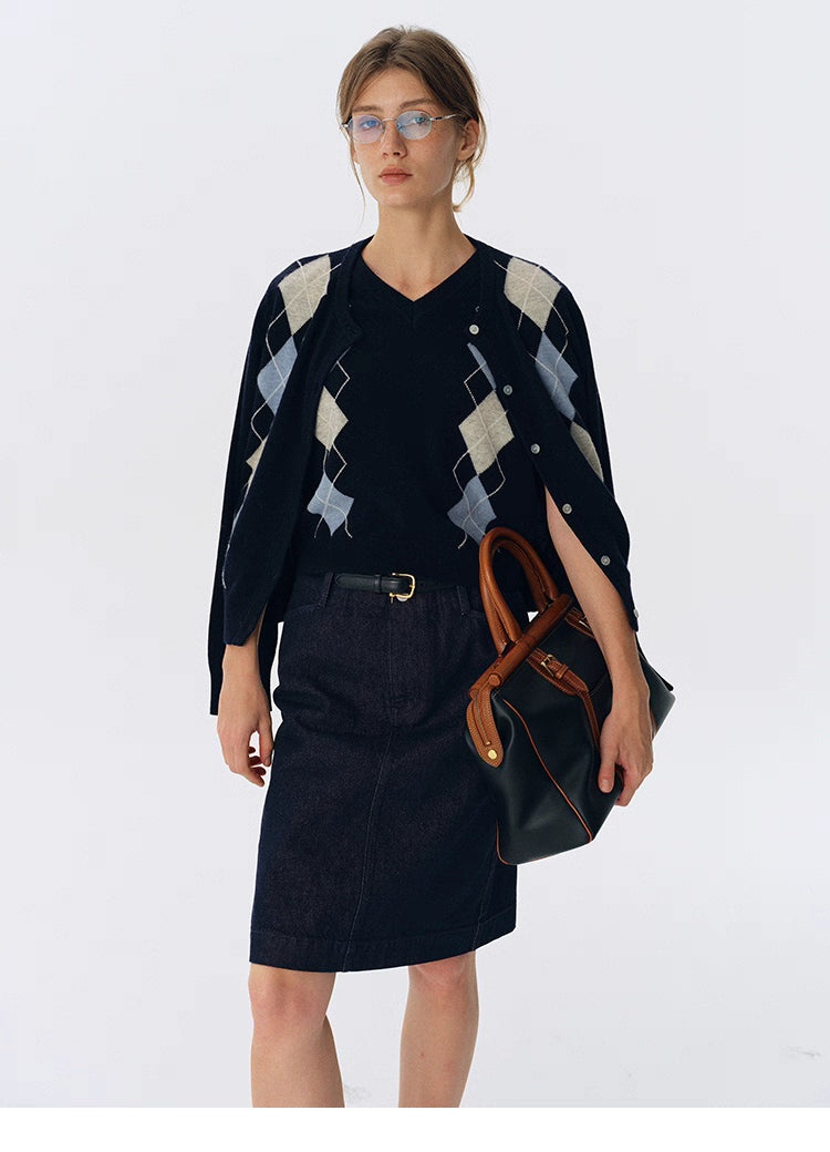 Navy wool argyle cardigan draped over shoulders on top of a navy V-neck sweater, styled with a denim skirt and black belt.