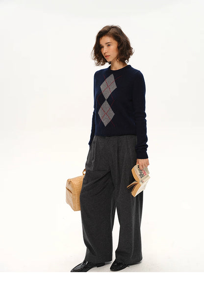 Full body shot of navy argyle wool sweater styled with gray wide-leg pants and a woven tote bag.
