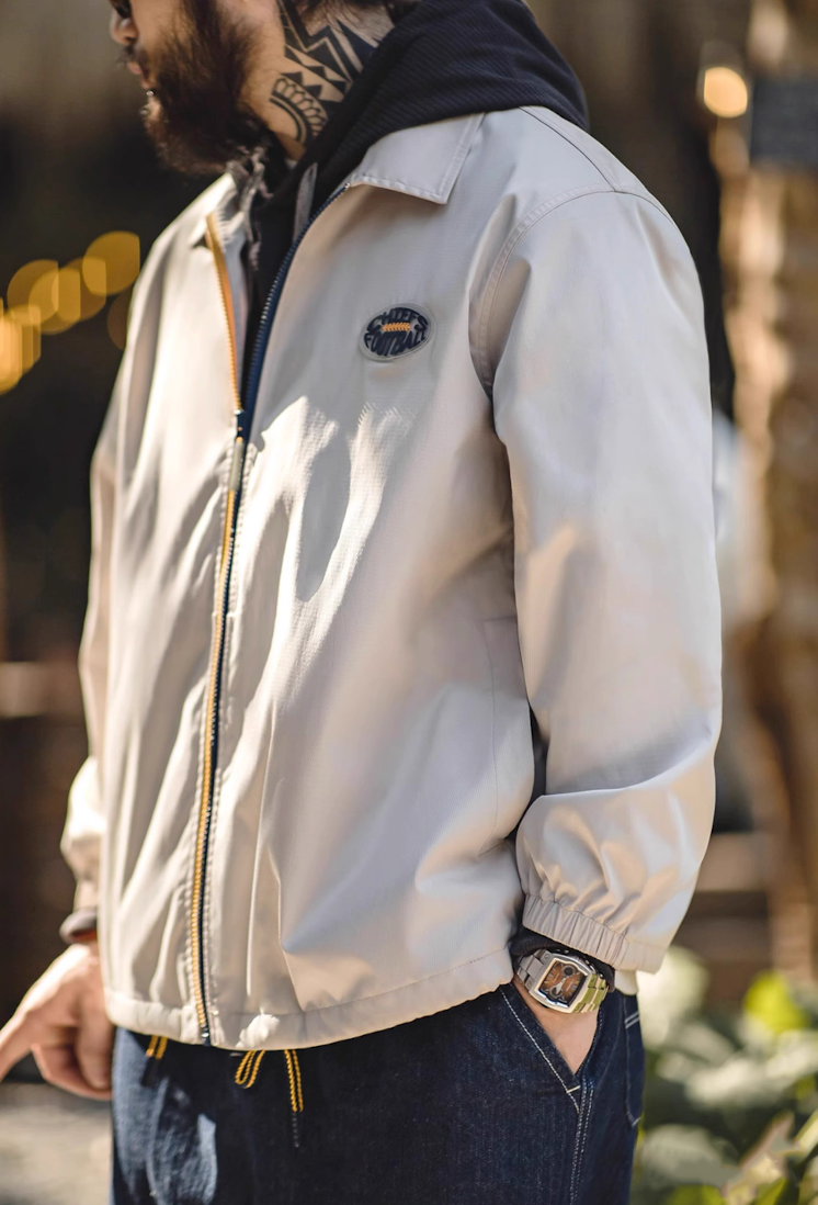 Side profile of man in off-white coach jacket with hoodie, hands in pocket.