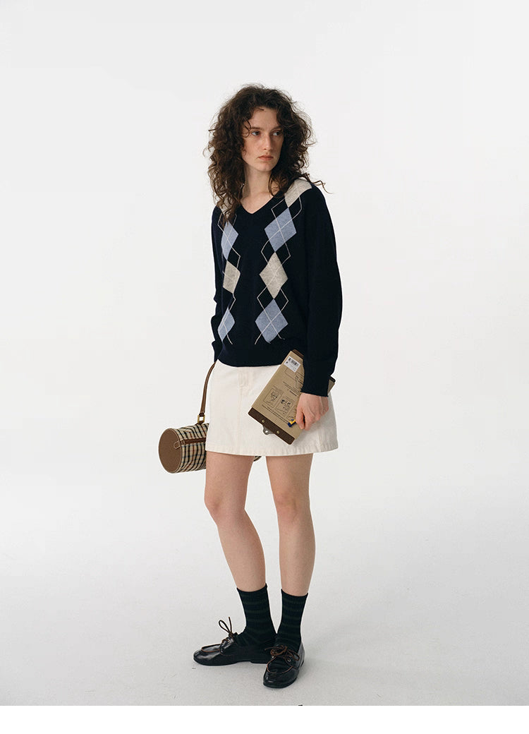Full body shot of navy argyle V-neck wool sweater styled with white skirt and black loafers.