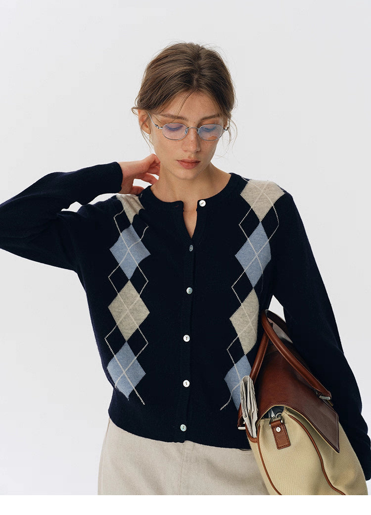 Front view of navy blue argyle wool button-up cardigan, paired with a beige skirt and structured bag.