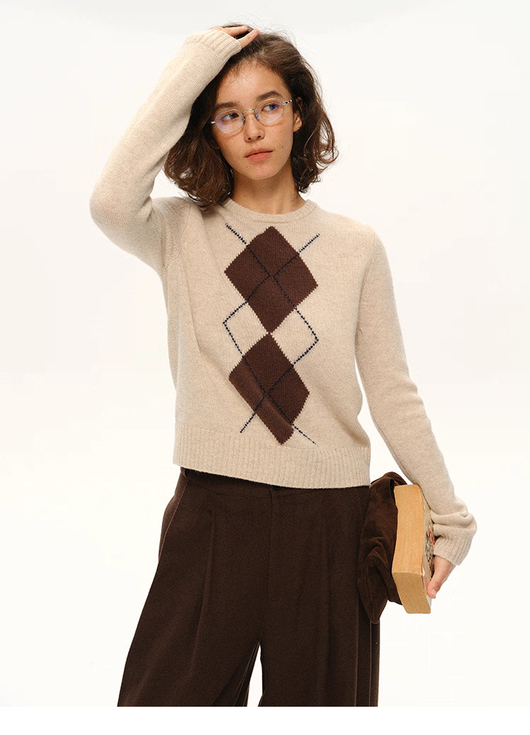 Front view of model wearing beige 100% wool argyle crewneck sweater with glasses and brown trousers.
