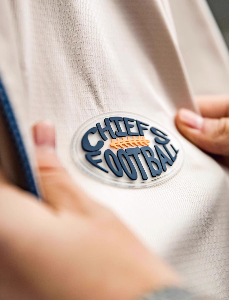 Close-up of Chiefs Football patch logo on off-white coach jacket chest.