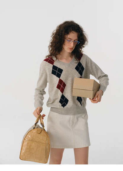 Front view of oat gray V-neck wool sweater with burgundy and navy argyle, model holding a box.