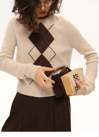 Close-up of beige argyle wool sweater as the model holds a brown suede pouch and a book at the waist.