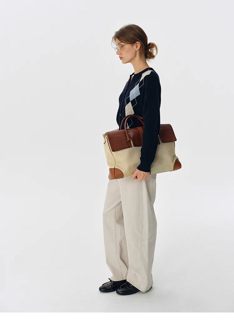 Side full-body shot of navy argyle wool cardigan styled with wide-leg beige pants and a canvas-and-leather work bag.