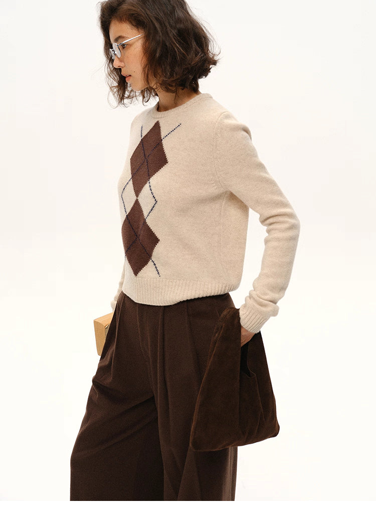 Side view of beige wool argyle sweater paired with brown wide-leg pants and a suede handbag.