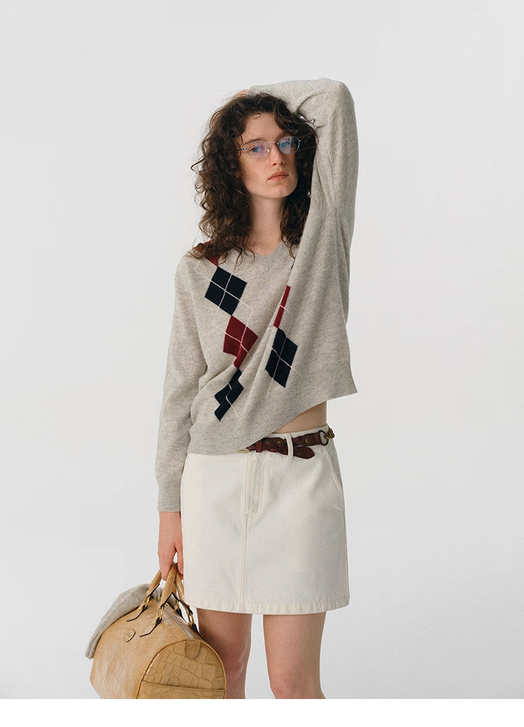 Full body shot of oat gray argyle wool sweater paired with white skirt and beige leather bag.